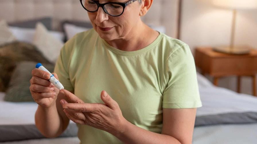 Mujer adulta realizándose una prueba de glucosa en sangre para detectar diabetes. La imagen muestra a la señora mirando su dedo mientras recibe asistencia para la prueba, simbolizando la importancia de los chequeos preventivos en el control de la diabetes.